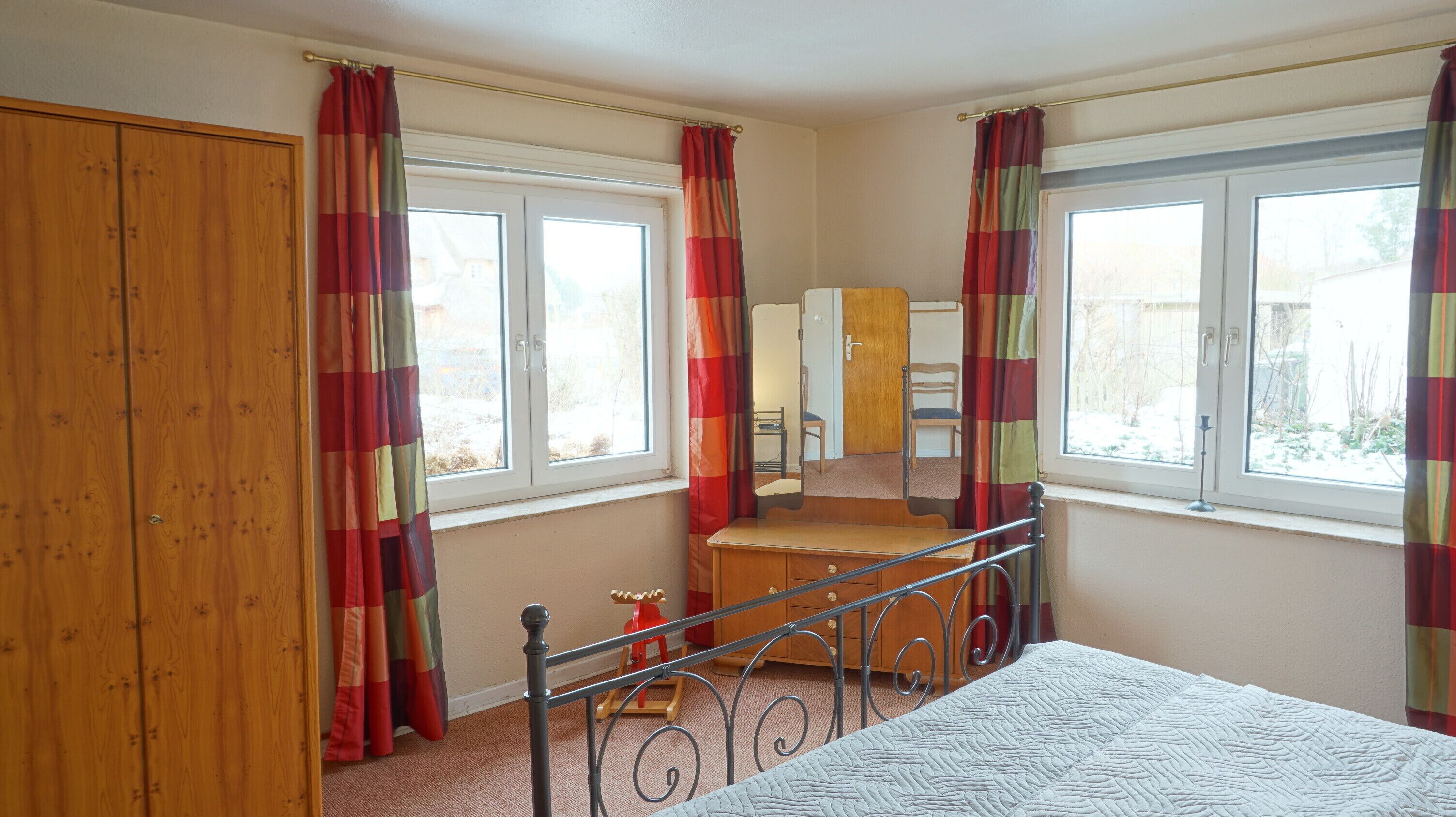A bedroom with a bed, a wooden wardrobe, a desk, and a chair.