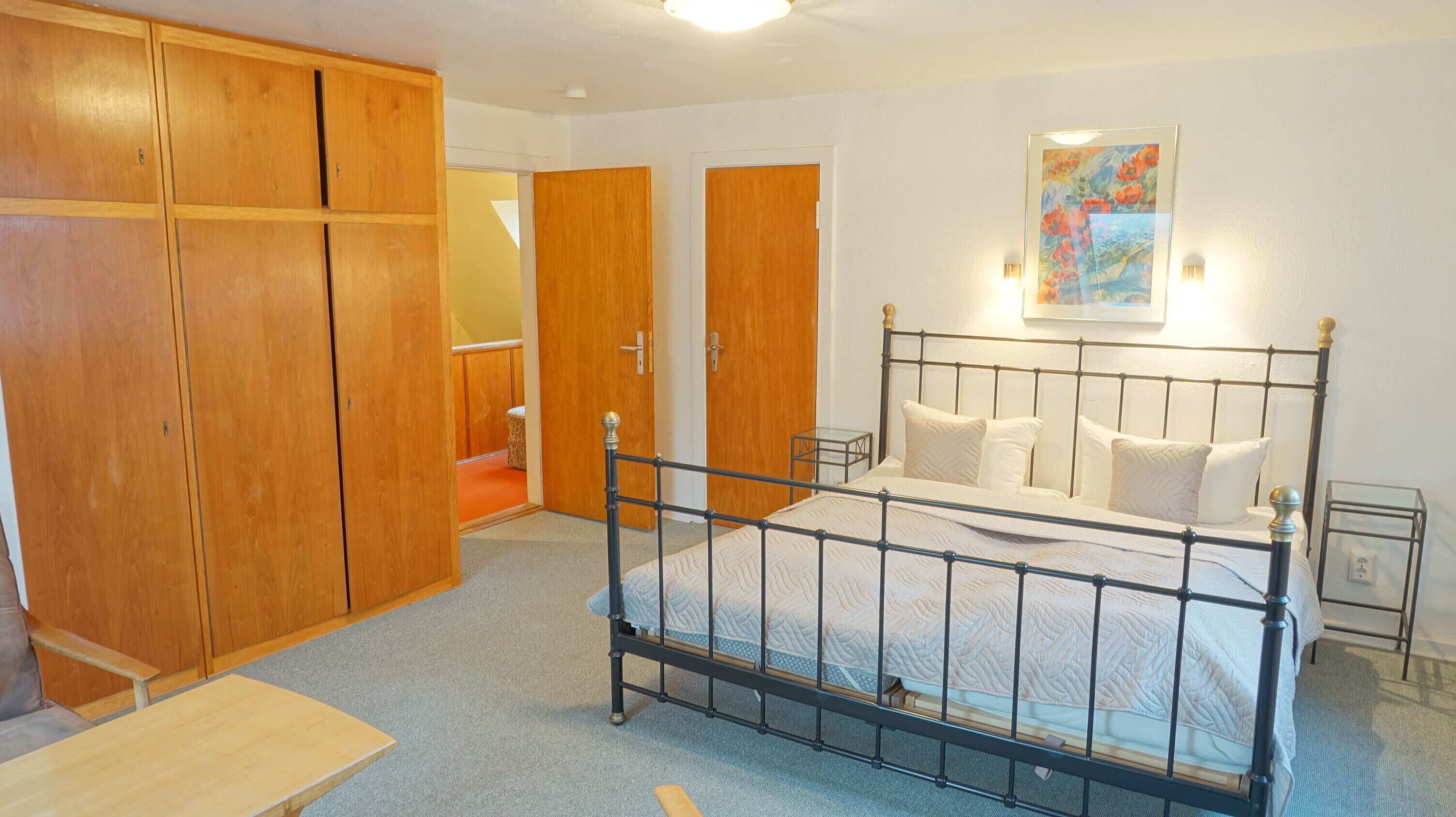 A bedroom with a metal-framed bed, wooden wardrobe, and a small bedside table.