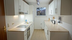 A compact kitchen with white cabinets, a built-in oven, a sink, and a window with a view of trees.