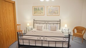 A bedroom with a metal bed frame, two bedside tables with lamps, a wooden chair, and two framed paintings on the wall.