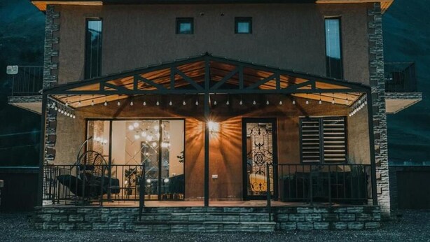 A two-story building with a covered patio area, stone facade, and a mountain backdrop.