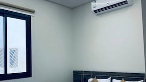 Una habitación de hotel moderna con una cama grande, una ventana con persianas, un equipo de aire acondicionado y una lámpara de techo.