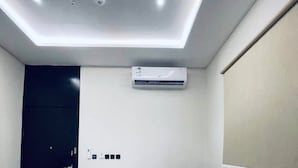 Una sala de estar moderna con un sofá seccional, iluminación empotrada en el techo, un equipo de aire acondicionado y una puerta oscura.