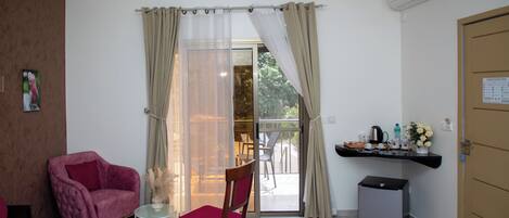 A room with a bed, a chair, a small table, a kitchenette, and a sliding glass door to an outdoor area.