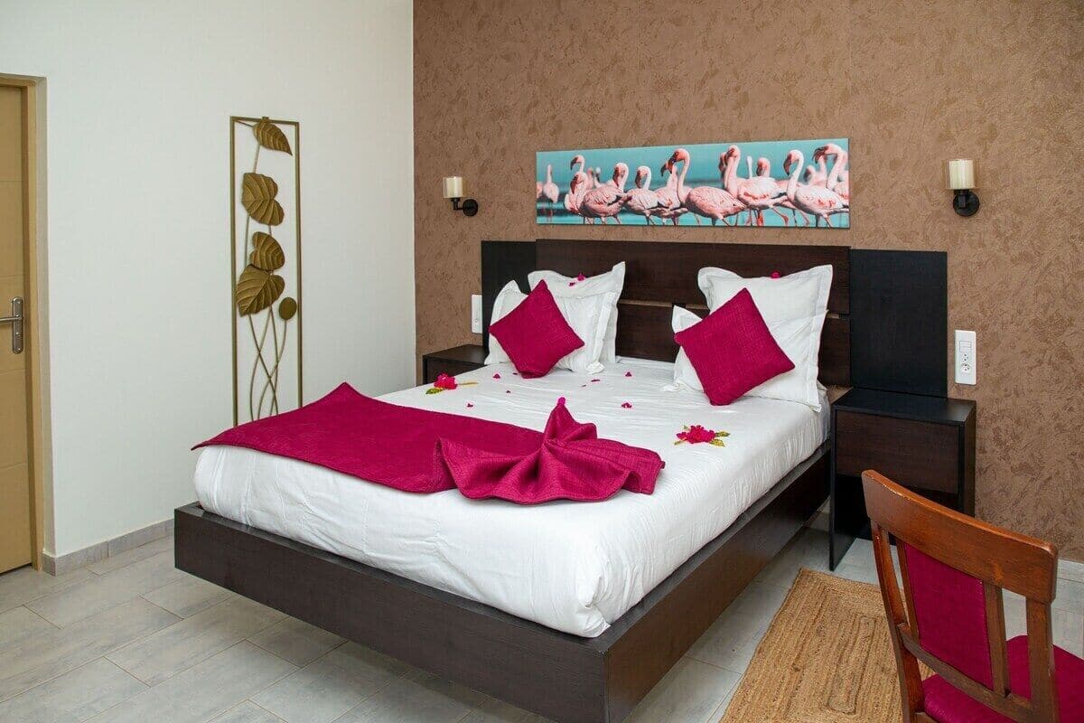 Une chambre d’hôtel comprenant un lit, une table de chevet, une chaise, une œuvre d’art représentant des flamants roses accrochée au mur, et un élément décoratif mural.