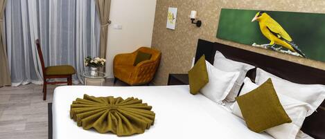 A hotel room with a bed, a chair, a small table with a vase, and a painting on the wall.