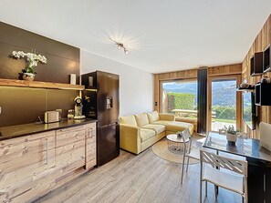 A modern kitchen with a built-in refrigerator, a wooden countertop, and a dining area with a table and chairs. - 2-room apartment with mountain corner, parking, Mont Blanc view (Combloux)