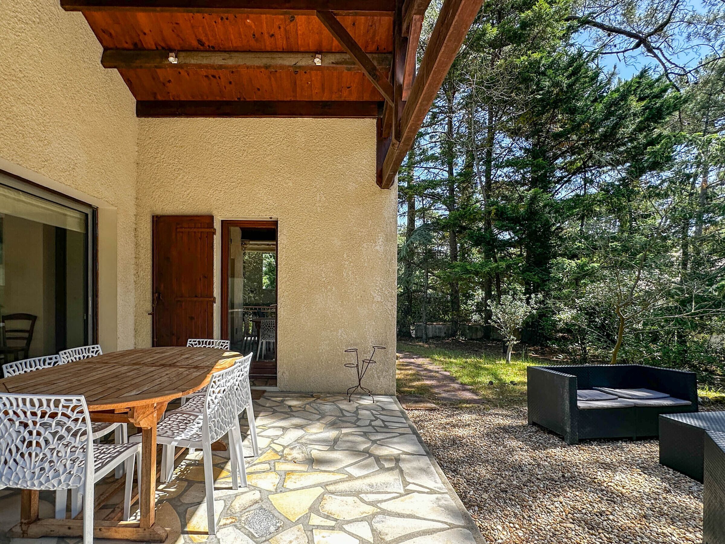 Una terrazza esterna con tavolo e sedie di legno, pavimento in pietra e vista su una zona boschiva.