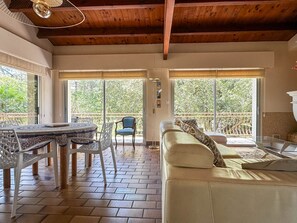A spacious living area with a sofa, a dining table with chairs, and large windows offering a view of greenery. - Spacious villa for 10 guests - Park - Wi-Fi, Air Conditioning (La Palmyre)