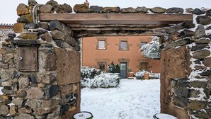 Ein Steingewölbe führt zu einem Gebäude mit einem schneebedeckten Garten und einer Holzpergola.
