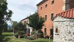 Ein Steinhaus mit rotem Ziegeldach, umgeben von einem Garten mit verschiedenen Pflanzen und einem Pfad.