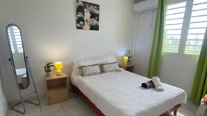 Een netjes opgemaakt slaapkamer met een bed, bedlampjes, een spiegel, een klein tafeltje met een plant en een aan de muur hangend schilderij.