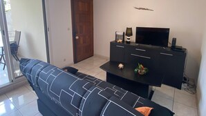 Een woonkamer met een zwarte bank, een televisie op een zwarte kast, en een deur aan de linkerkant.