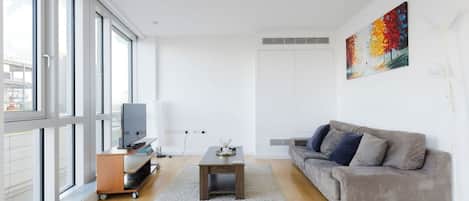 Una sala de estar moderna con un sofá gris, una mesa de centro, un televisor sobre un mueble de madera y un cuadro en la pared.