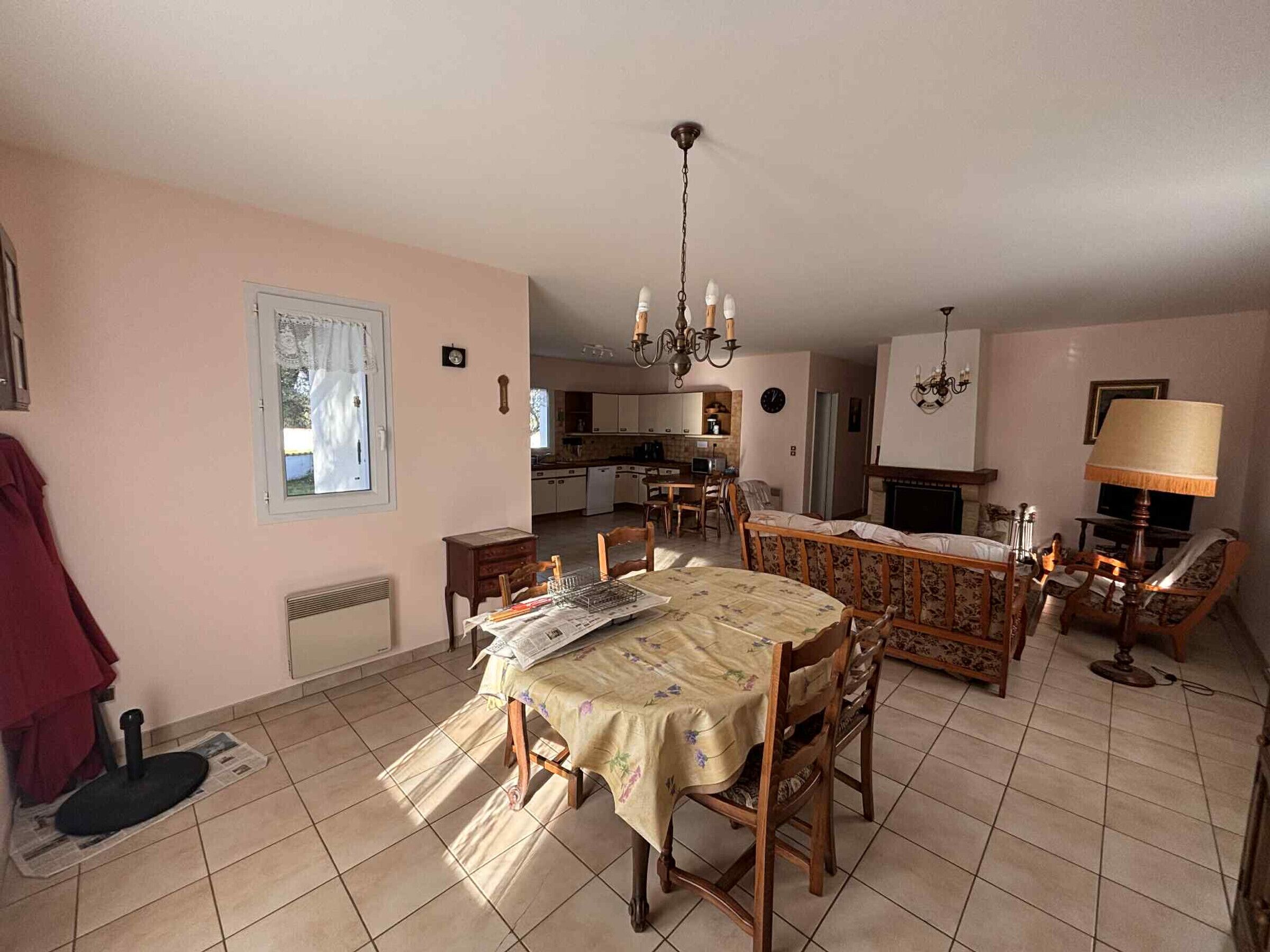 Een ruime woonkamer met een eettafel, stoelen, een open haard en een keuken op de achtergrond.