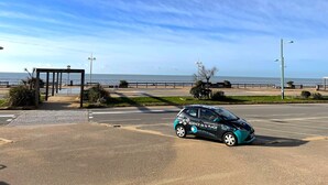 Uma área de estacionamento com um carro, uma passarela para pedestres e vista para o mar.