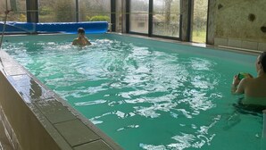 En inomhuspool med väggar av genomskinligt glas, en blå uppblåsbar poolleksak och en person som håller i en boll.