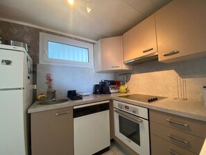 Eine kompakte Küche mit integriertem Geschirrspüler, Backofen, Spüle und einem Fenster über der Arbeitsfläche.