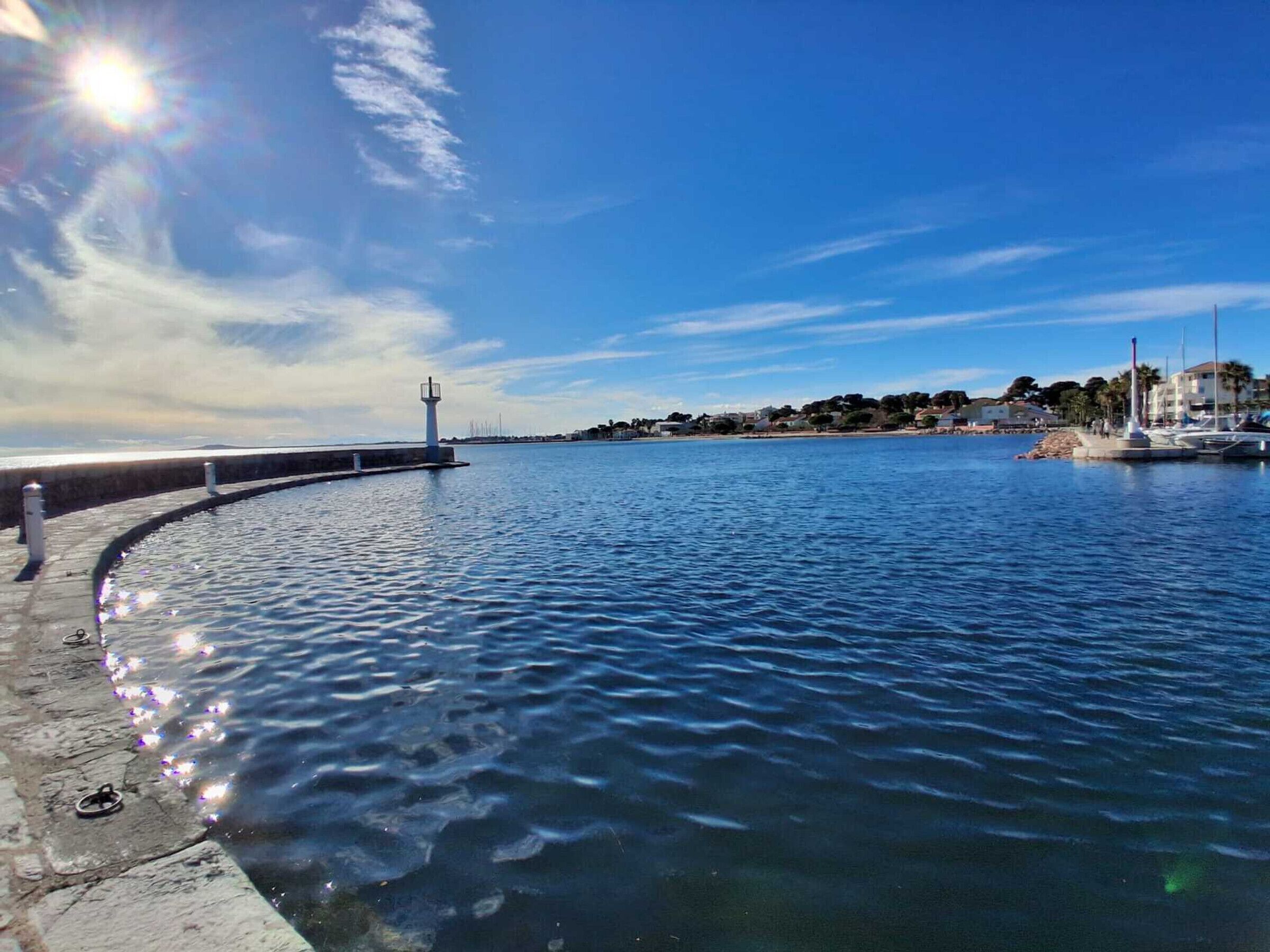 A waterfront marina with a curved dock, a lighthouse, and boats.