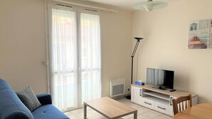A living room with a blue sofa, a wooden coffee table, a TV on a wooden stand, and a floor lamp. - Central Apartment for 4 - Parking Included (Royan)