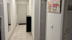 A hallway with a tiled floor, a black cabinet, a door, and a wall-mounted artwork. - Central Apartment for 4 - Parking Included (Royan)