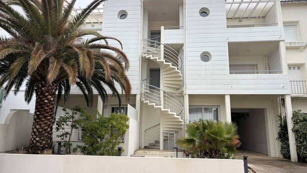 A modern building with a central spiral staircase, multiple balconies, and a palm tree in the foreground. - Central Apartment for 4 - Parking Included (Royan)