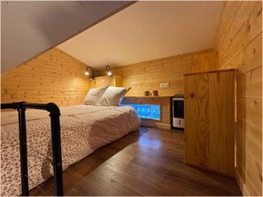 Ein gemütliches Schlafzimmer im Dachgeschoss mit holzgetäfelter Schräge, einem Bett mit Blumenmuster und einem kleinen Fenster für natürliches Licht.