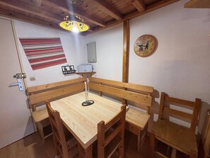 A dining area with a wooden table and benches, a hanging light fixture, a striped wall hanging, and a clock on the wall. - 2-room Apartment with Cabin in Les Angles, close to shops (Les Angles)