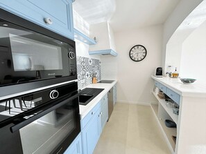 A compact kitchen with a built-in oven, microwave, and a wall clock. - 2-Bedroom Apartment with Air Conditioning and WIFI (Port Grimaud)
