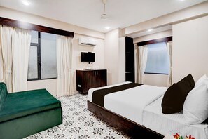 Une chambre d’hôtel avec un lit, un canapé vert, une télévision et un appareil de climatisation.