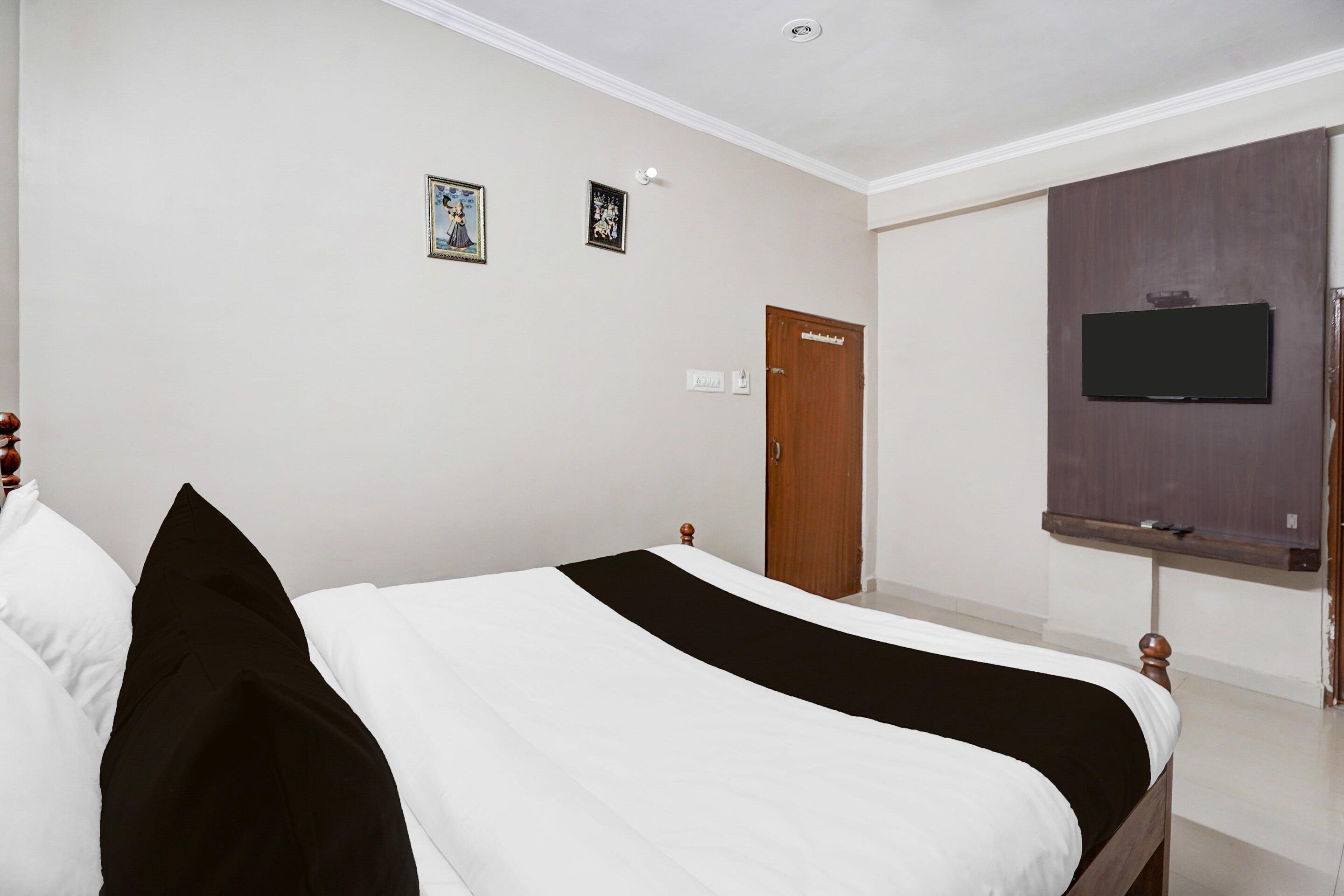 Quarto com cama, televisão na parede e porta.