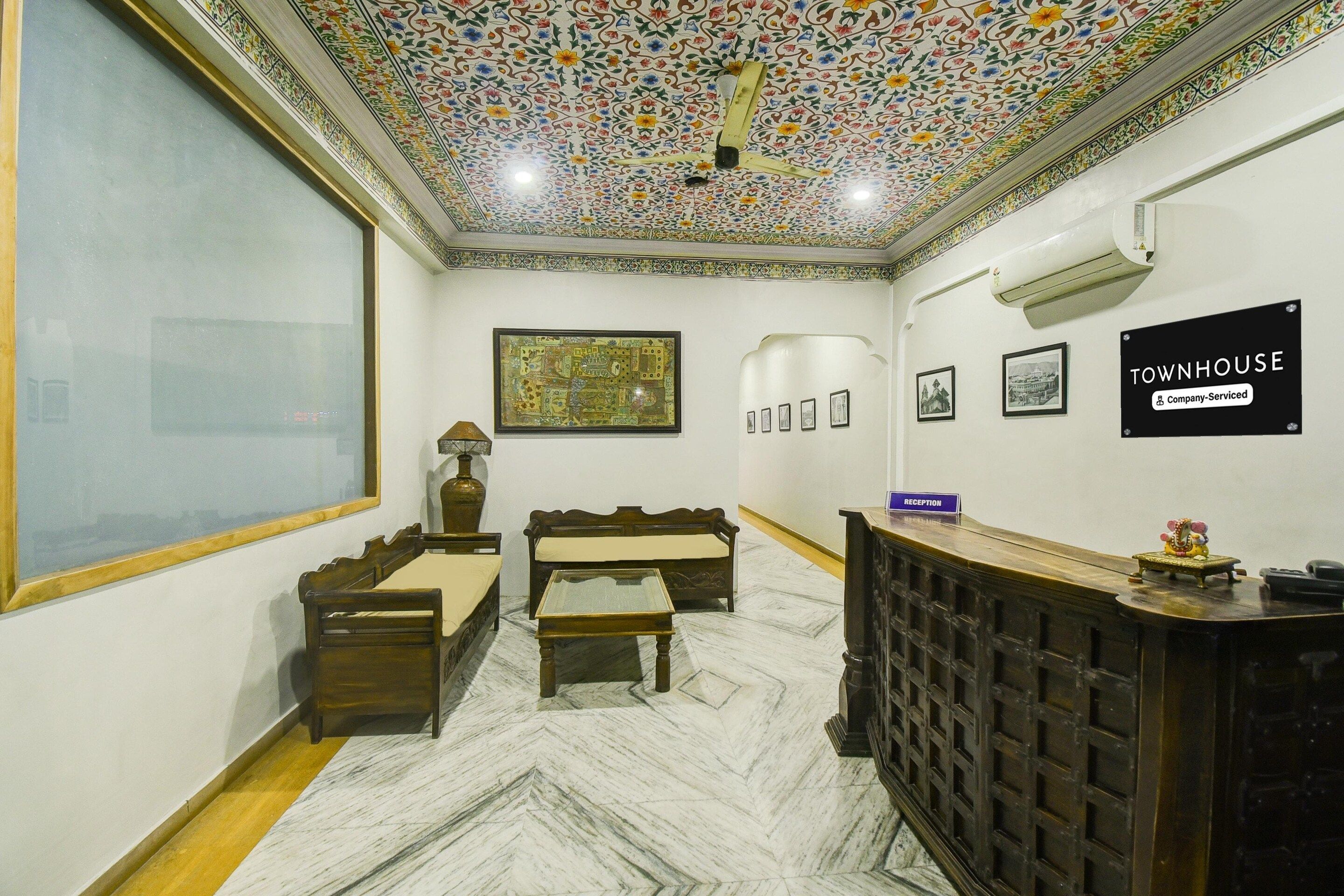 Un espace d’accueil avec un plafond carrelé, un comptoir de réception, un canapé, une petite table et des tableaux encadrés accrochés au mur.
