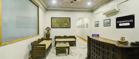 A reception area with a tiled ceiling, a reception desk, a sofa, a small table, and framed pictures on the wall.