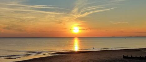 A beach with a sunset, a clear sky, and a calm sea.