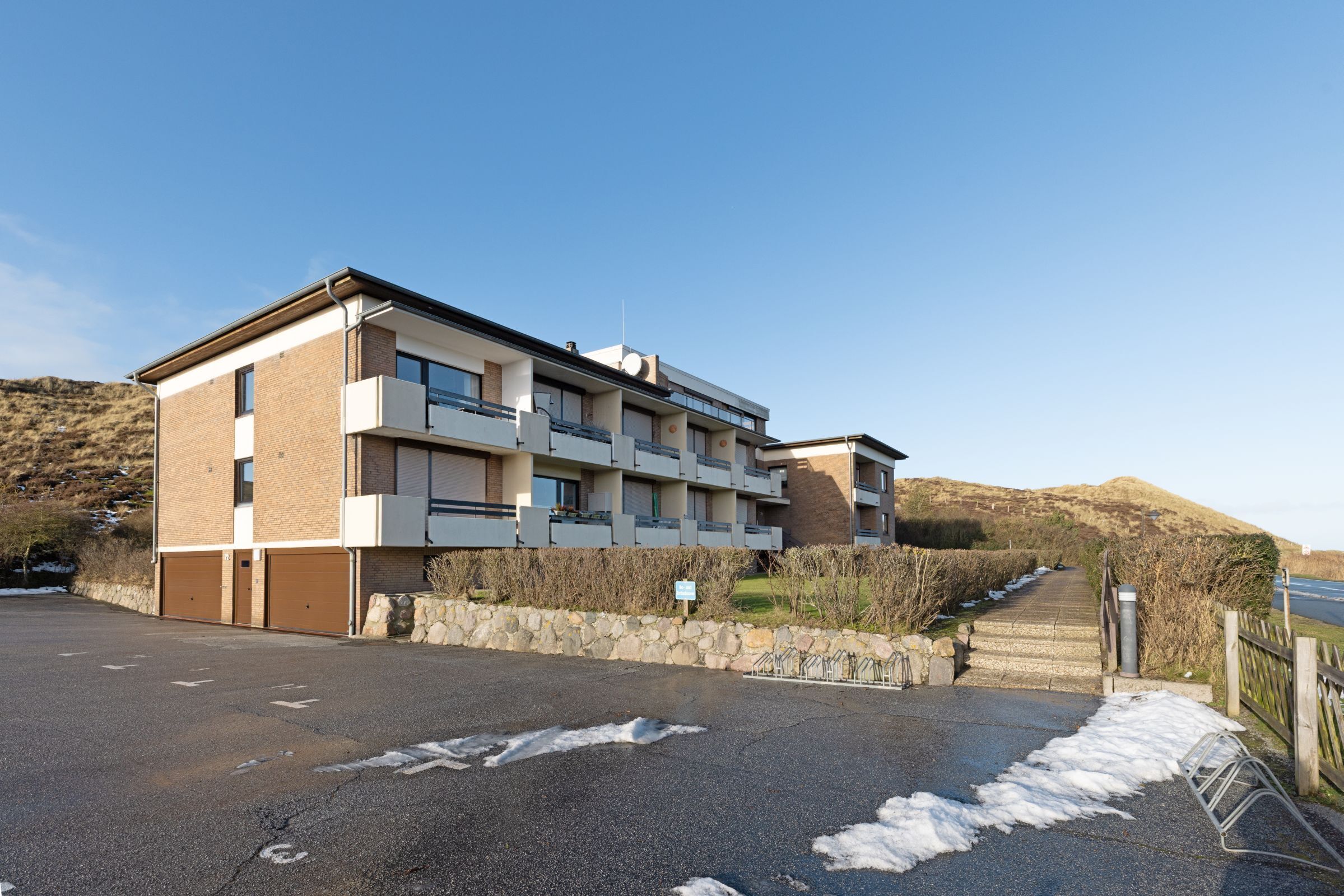 Un bâtiment moderne à plusieurs étages, doté d’un toit plat, de grandes fenêtres et d’un mur en pierre à l’avant.