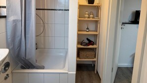 Kylpyhuone, jossa on suihku, wc ja hylly, jonka päällä on ruukussa oleva kasvi.