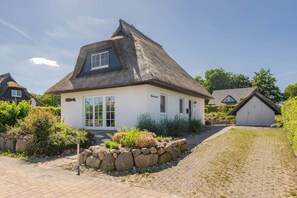Ett traditionellt hus med ett halmtak, en grund av sten och en asfalterad uppfart.