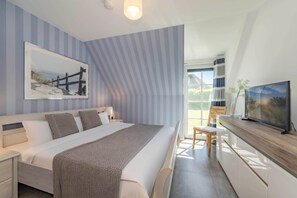 A modern hotel room with a large bed, a television, a desk, and a window with a view. - Luxurious thatched house in Zinnowitz - wellness, garden & fireplace (Zinnowitz)