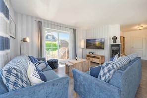 A living room with a sofa, a coffee table, a TV, and a fireplace. - Luxurious thatched house in Zinnowitz - wellness, garden & fireplace (Zinnowitz)