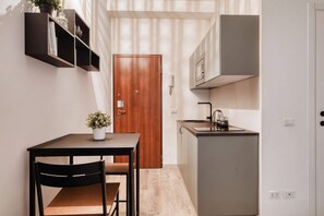 Eine kompakte Küche mit Holztür, einem kleinen Esstisch mit Stühlen, einem Topf mit Pflanze und einem eingebauten Schrank.