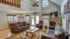 A spacious living room with a high ceiling, a fireplace, and a dining area with a chandelier.