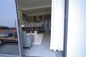 Una cocina moderna con gabinetes grises, horno integrado y refrigerador. En la sala de estar, hay un sofá gris y una alfombra blanca.