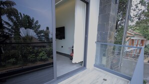 A balcony with a glass door leading to a room with a television, a small table, and a red chair. - Heritage Residences-Velvet Rouge 1BR (Kampala)