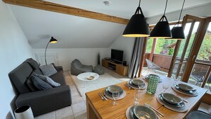 A dining area with a wooden table set for four, a grey sofa, and a television in the background.