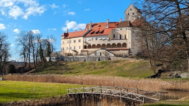 A historic building with a red-tiled roof, a central courtyard, and a bridge over a body of water.