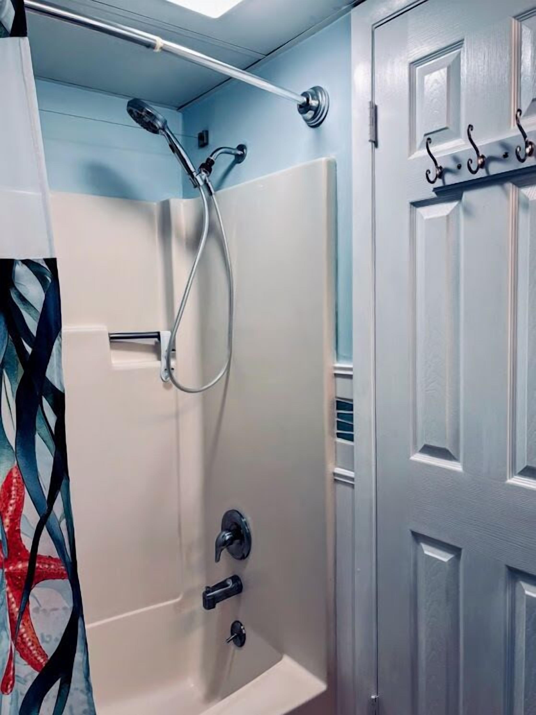 A bathroom with a shower, a bathtub, and a door with a coat rack.