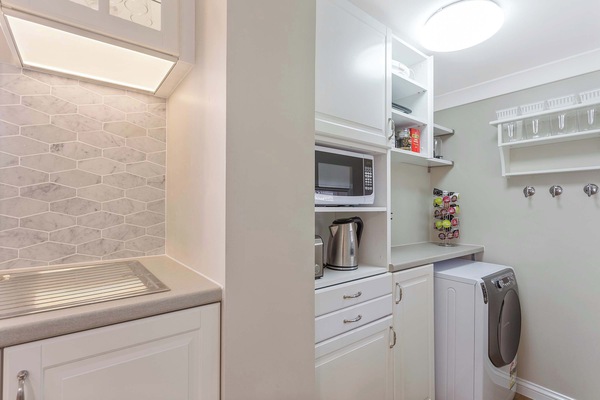 Compact laundry space with washer, dryer, shelving, and sink.