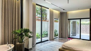 Una habitación de hotel moderna con una cama grande, una bañera y un ventanal corredero que da a un balcón.
