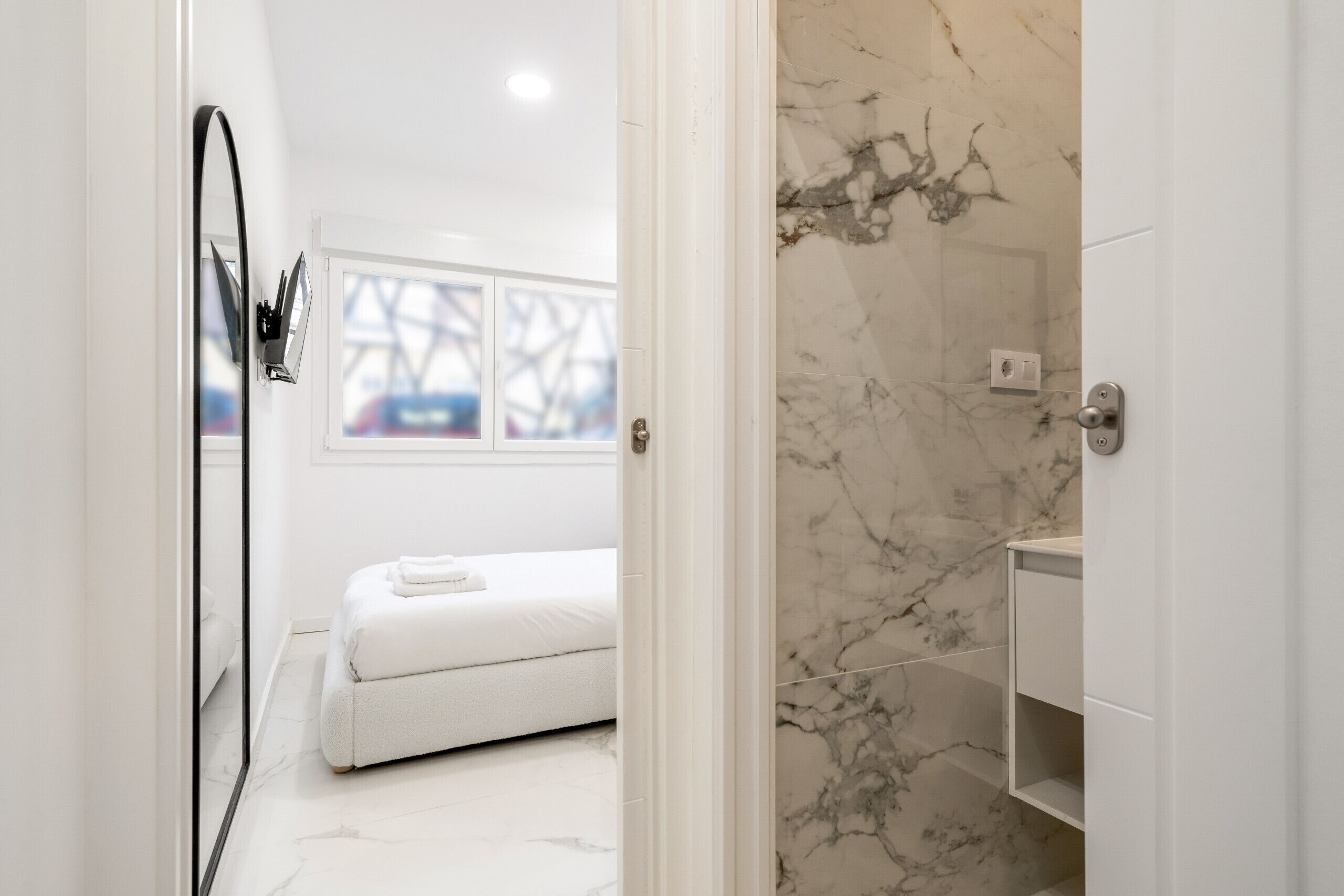A modern bathroom with a white bathtub, a marble shower wall, and a white vanity.