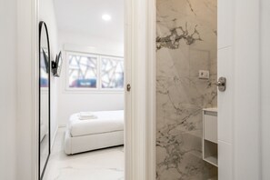 Un bagno moderno con una vasca da bagno bianca, una parete doccia in marmo e un mobile lavabo bianco.
